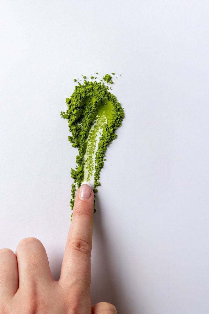 Matcha-Pulver wird mit dem Finger auf einem weißen Blatt Papier verschmiert